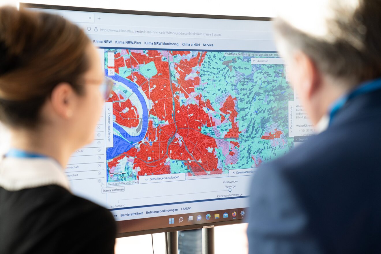 Zwei Personen vor dem Bildschirm des Klimastandes bei dem Forum Klimaresilienz 2023. Zu sehen ist die Klimaanalyse vom Klimaatlas NRW. Foto: Netzwerkt Klimaanpassung und Unternehmen
