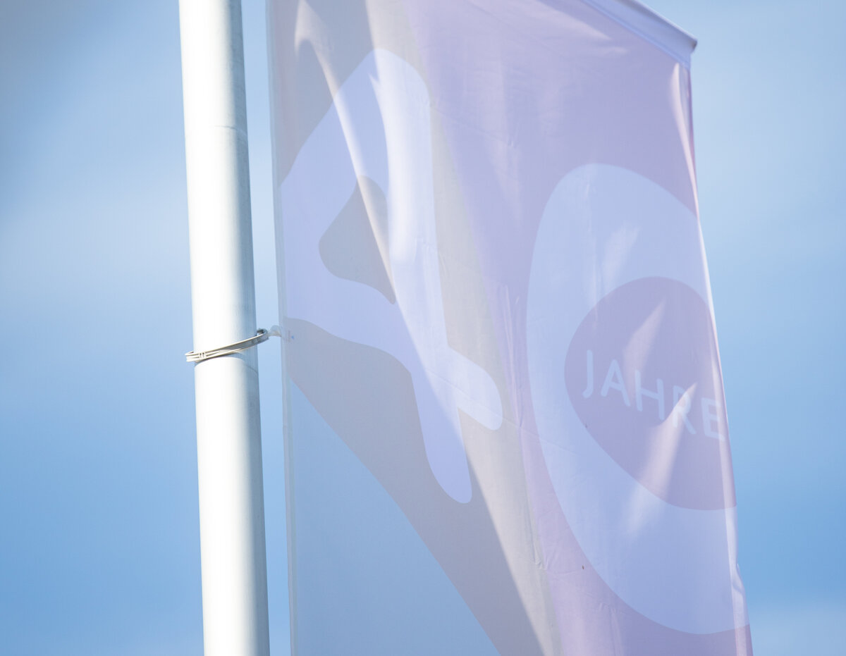 Eine Fahne in Pastellfarben mit dem Aufdruck "40 Jahre" weht vor blauem Himmel