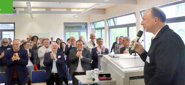 Das Auditorium klatscht Beispielfür Michael Jöbges, der am Rednerpult mit dem Mikrophon in der Hand steht.
